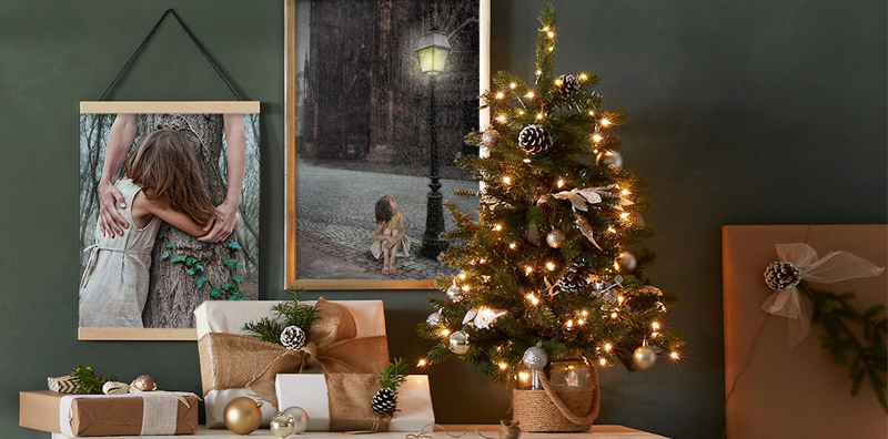 Étagère avec sapin de cadeaux de Noël, au mur deux photographies.