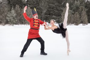 Photographie homme déguisé en Casse-noisette à côté d'une jeune ballerine en tutu noir dans un décor de neige.