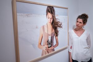 Une femme regarde une grande photographie encadrée d'une jeune fille qui tient un vieil appareil photo dans la neige.