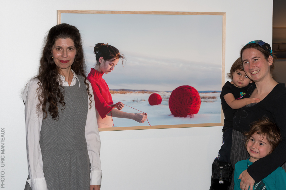 exhibition opening photograph showing artist photographer Catherine Rondeau, one of her works and a women with two children smiling