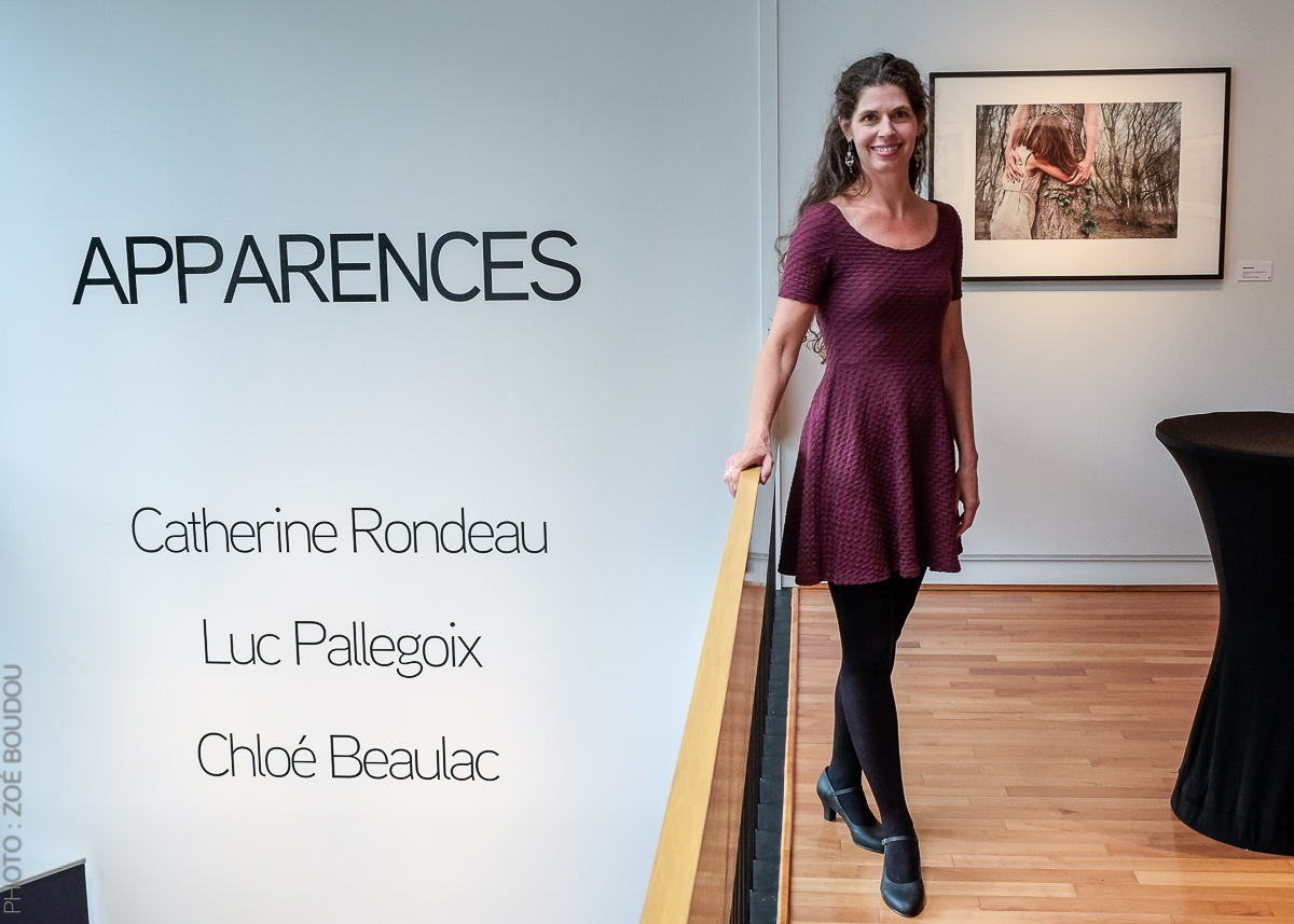 artist Catherine Rondeau stands in front of her photograph at an opening reception