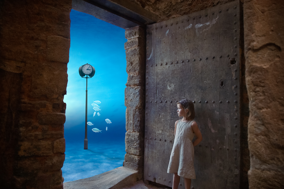 surreal tableau with little girl looking at fish swimming underwater through a door