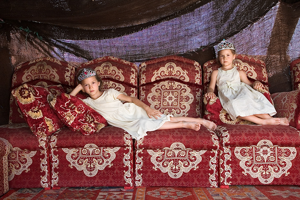 Two children sit like queens on a red marocain sofa