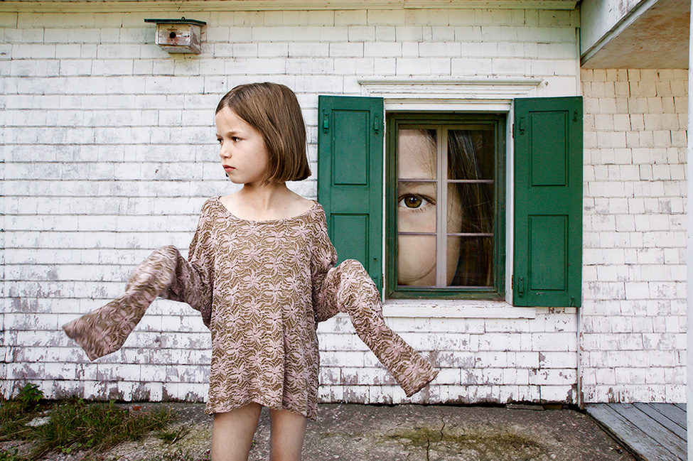 Photographie d'une surréaliste d'une enfant qui porte un vêtement ample devant une façade de maison