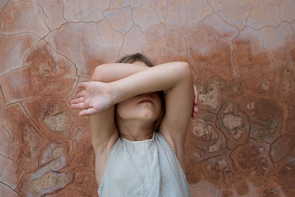 Photo of a child hiding her face behind her crossed arms