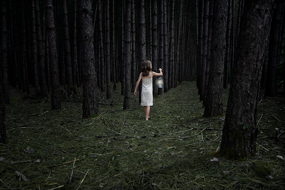 Photo of a child walking into the woods holding a lantern