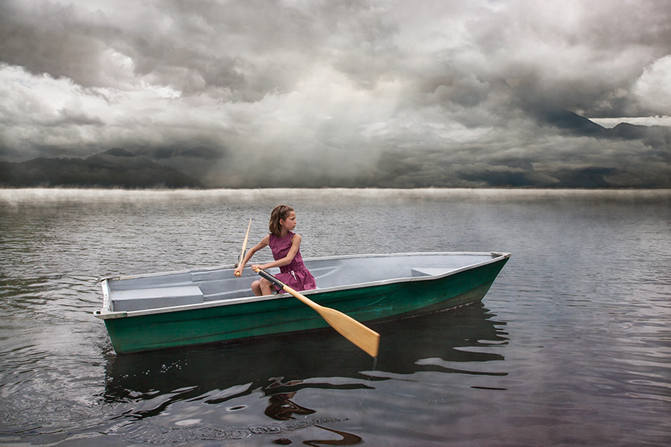 Photographie d'une enfant qui rame dans un lac sous un ciel sombre