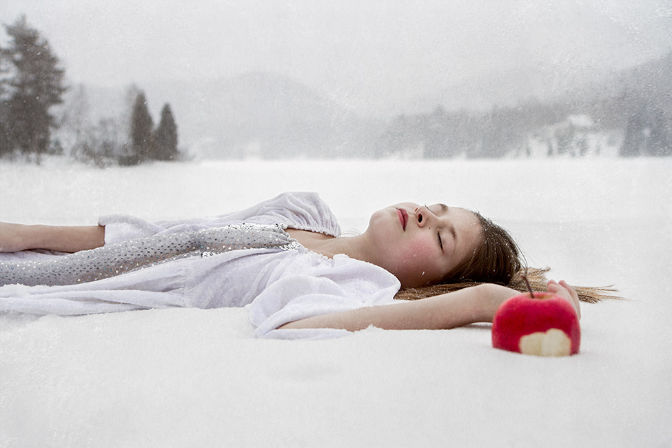 Photographe of a child laying in the white snow with a apple nearby