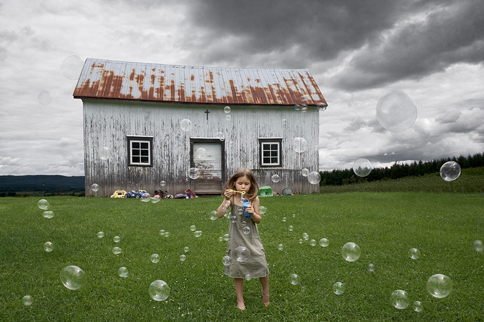 Photo montage of a child blowing soap bubbles in front of na old barn