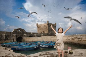 Photographie d'une enfant qui monte les bras dans les airs en imitant le vol des oiseaux qui l'entourent