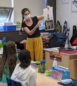 a woman shows a picture at the front of a classroom in an elementary school