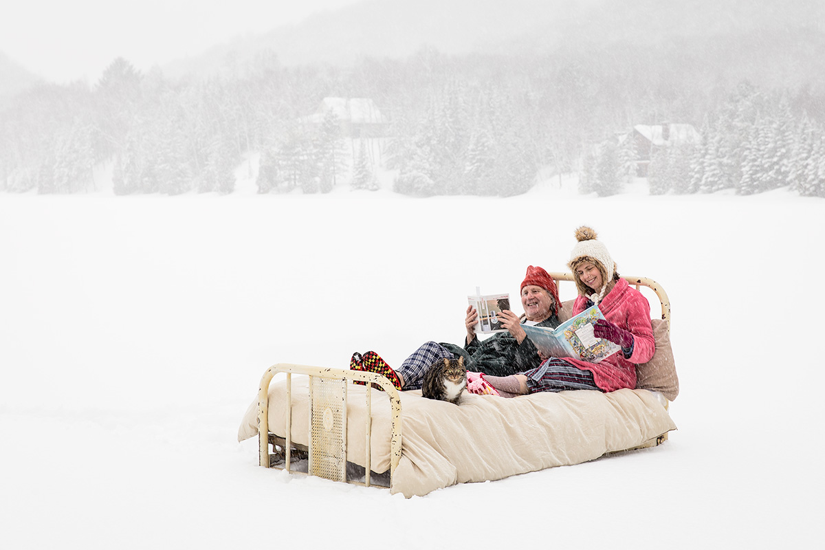 Un homme et une femme lisent sur un lit placé sur un lac enneigé.