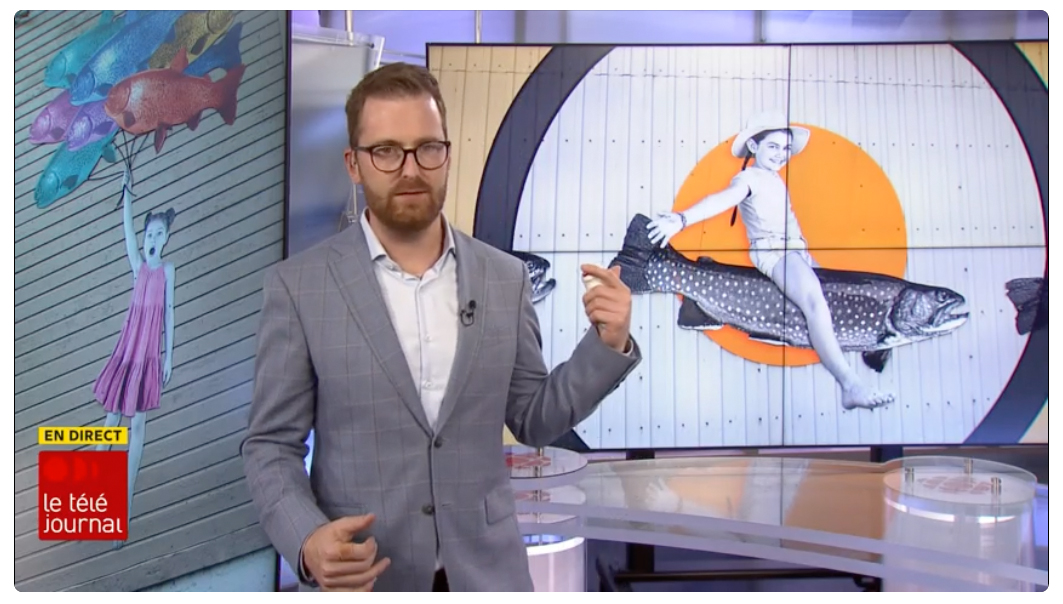 Un homme pointe un écran derrière lui où l'on voit un photomontage d'une enfant qui chevauche une truite. Le texte suivant est incrusté dans le coin gauche : EN DIRECT Téléjournal.